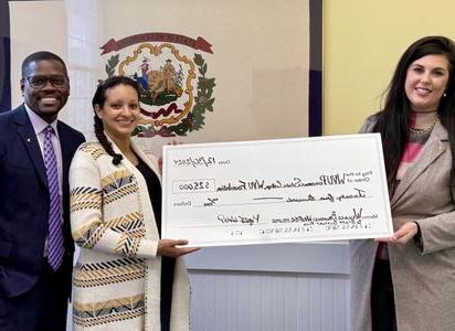 a photograph of Megan Webb, Allyson Wallace, and Jerry Wallace smiling at the camera as Megan and Allyson hold up a 25,000$ check for display